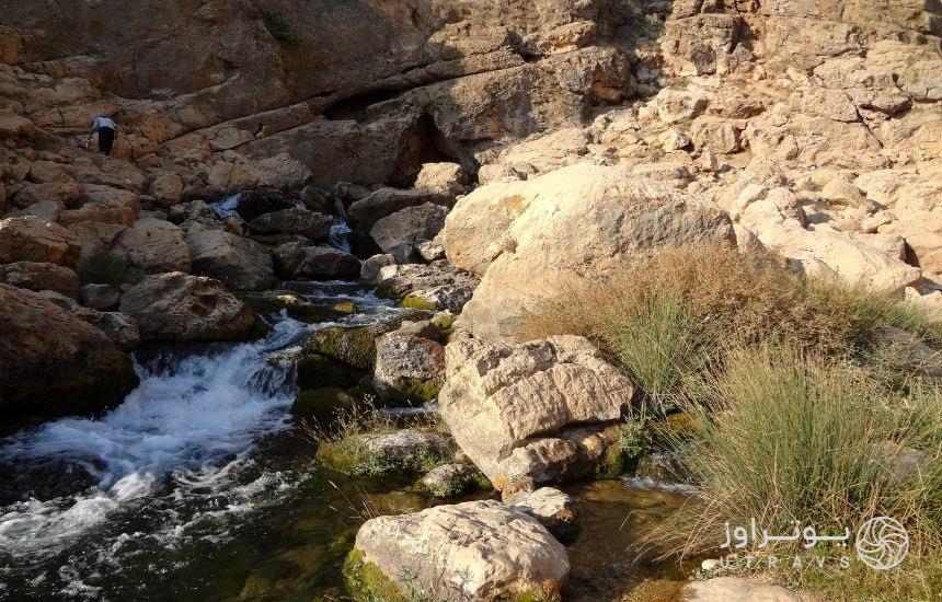 مسیری کوهستانی که چشمه‌ای آب در آن جاری است و در انتهای تصویر، مردی درحال پیمودن مسیر دیده می‌شود. 